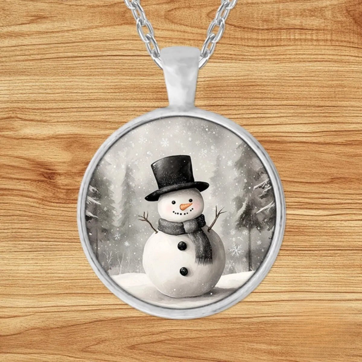 Round silver charm pendant necklace featuring a top-hat snowman with rosy cheeks and a carrot nose in a softly falling snowy forest
