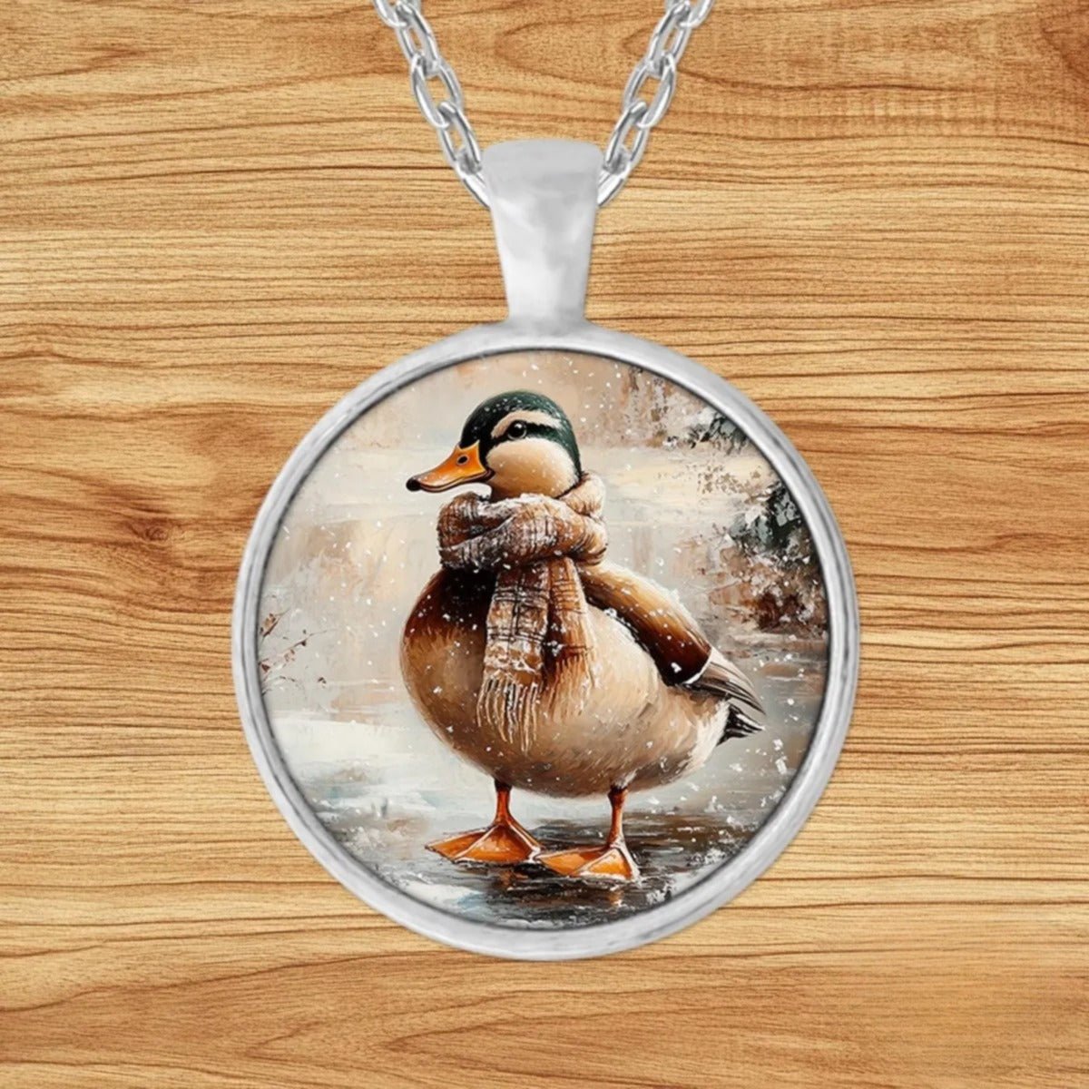 Round silver charm pendant necklace featuring a duck bundled in a plaid scarf standing on a frozen pond