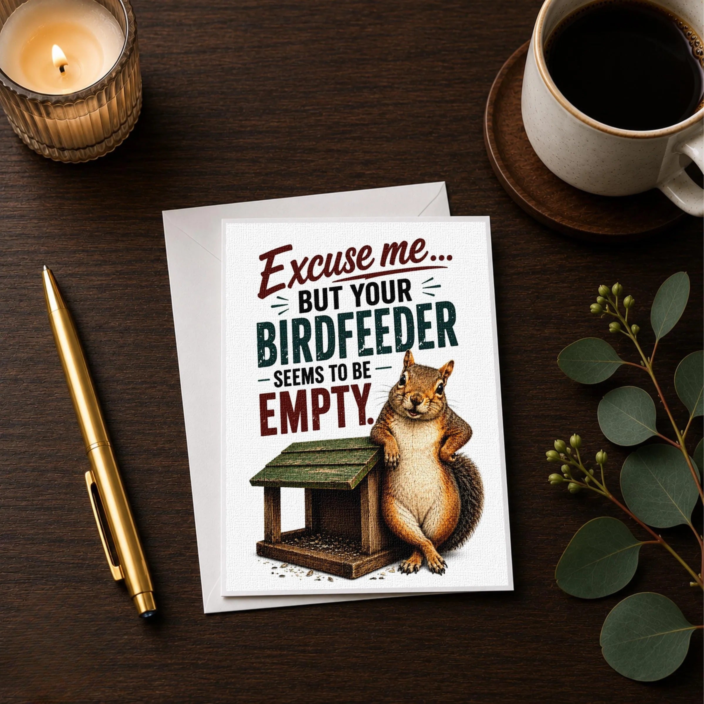 a greeting card with a squirrel sitting on a bird feeder, accompanied by a pen and a cup of coffee on a wooden surface.