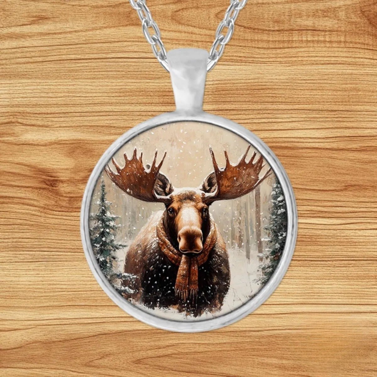 Round silver charm pendant necklace featuring an antlered moose bundled in a cozy plaid scarf in a snowy evergreen forest