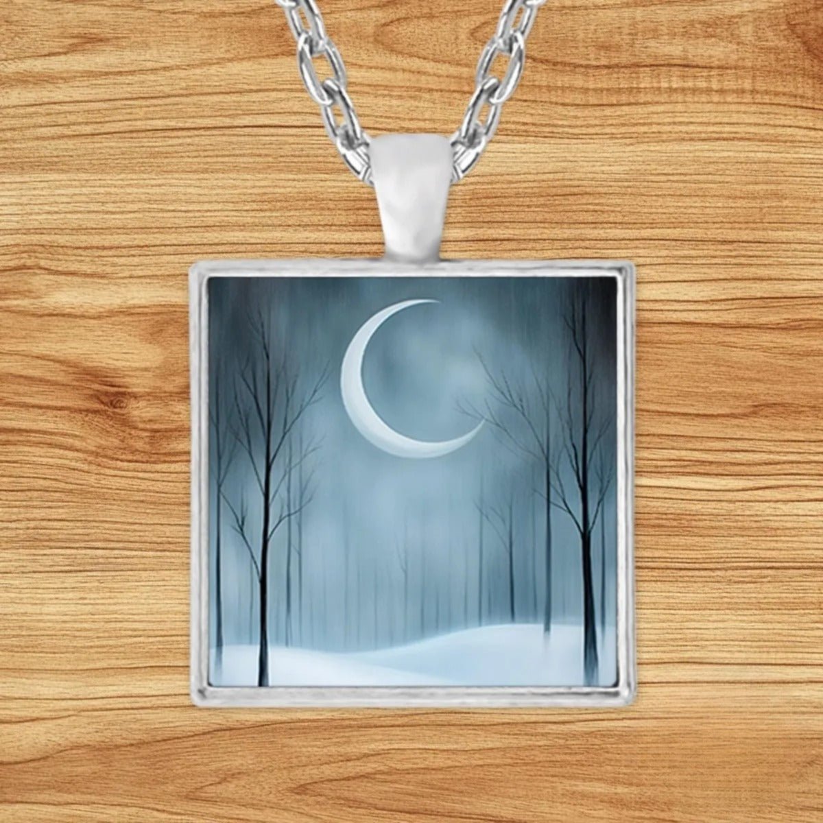 Square silver charm pendant necklace featuring a glowing crescent moon over a misty, snow-covered forest