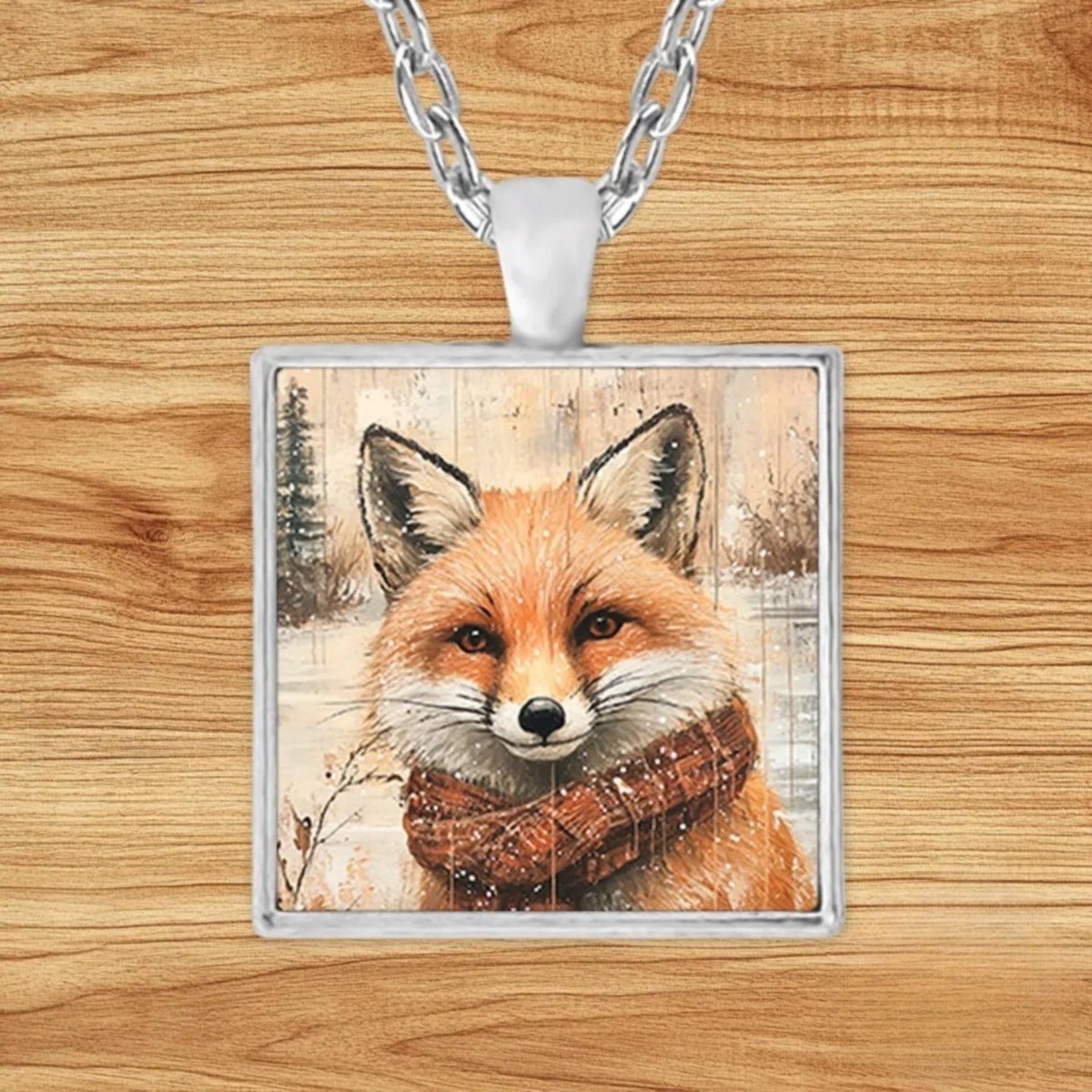 Square silver charm pendant necklace featuring a fox bundled in a red plaid scarf surrounded by falling snow and frosted pines