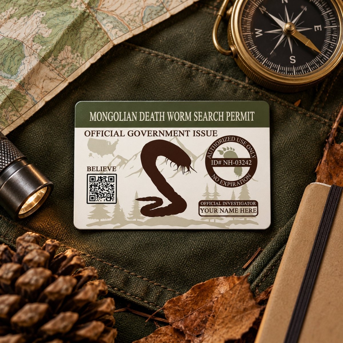 a "Mongolian Death Worm Search Permit" card, which is an official government issued document. The card is placed on a map, compass, and other outdoor gear, suggesting it is related to a search or investigation.