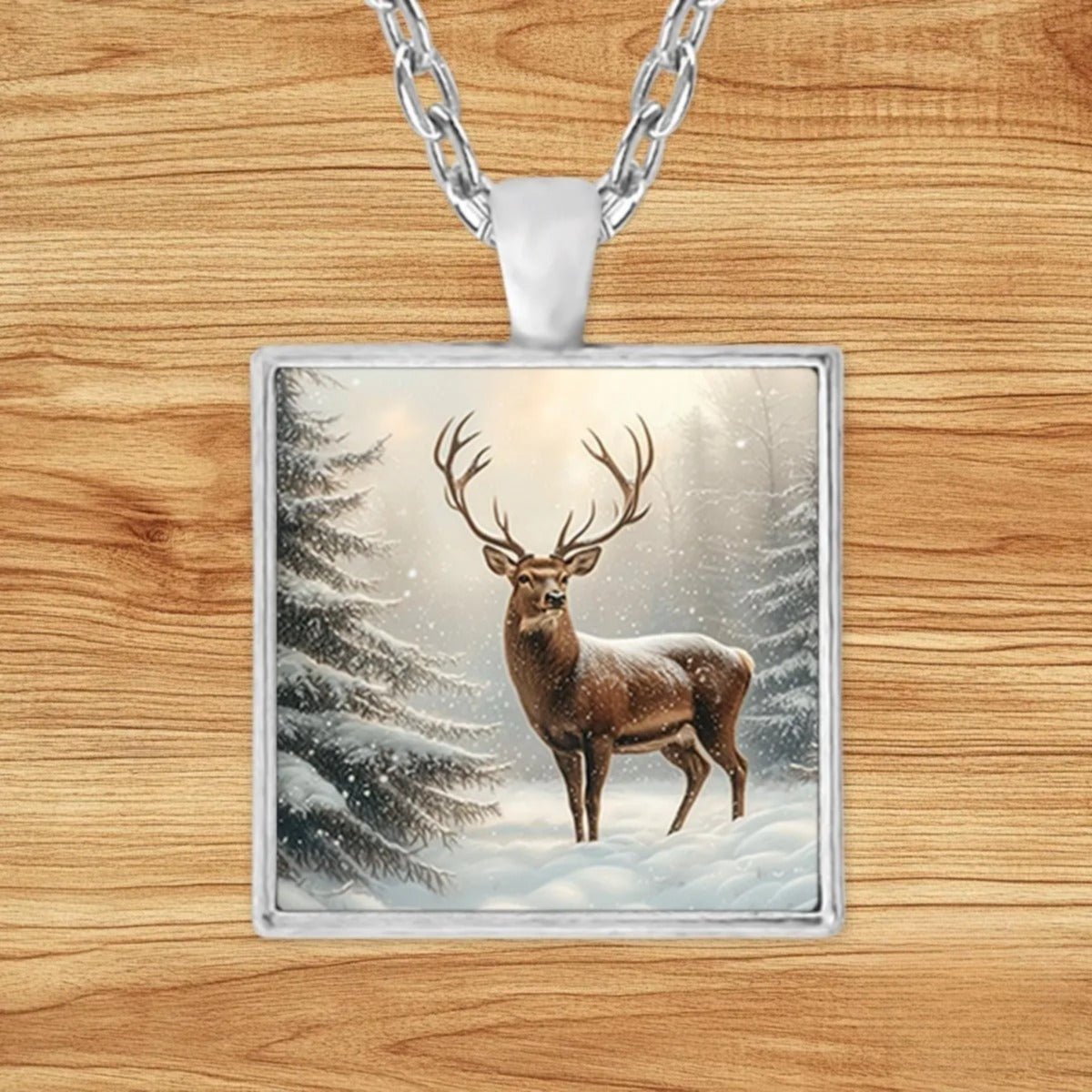 Square silver charm pendant necklace featuring a brown deer standing among towering snow-covered pines in soft winter light