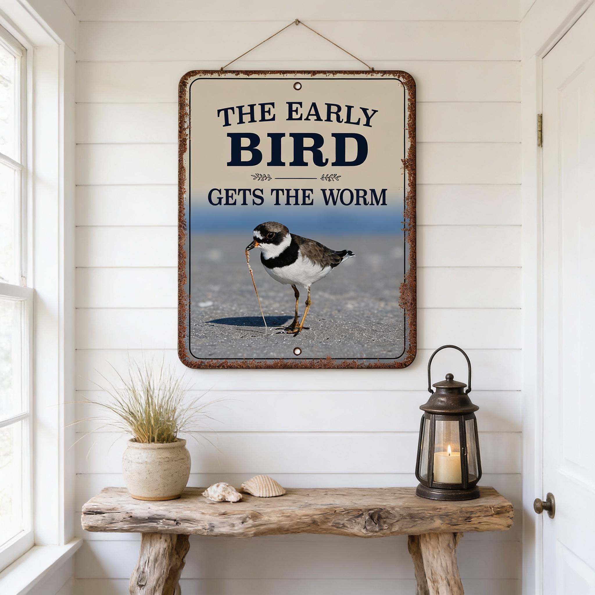 a rustic wooden table with a lantern, a potted plant, and a bird figurine on it. Above the table, there is a framed sign that reads "The early bird gets the worm".