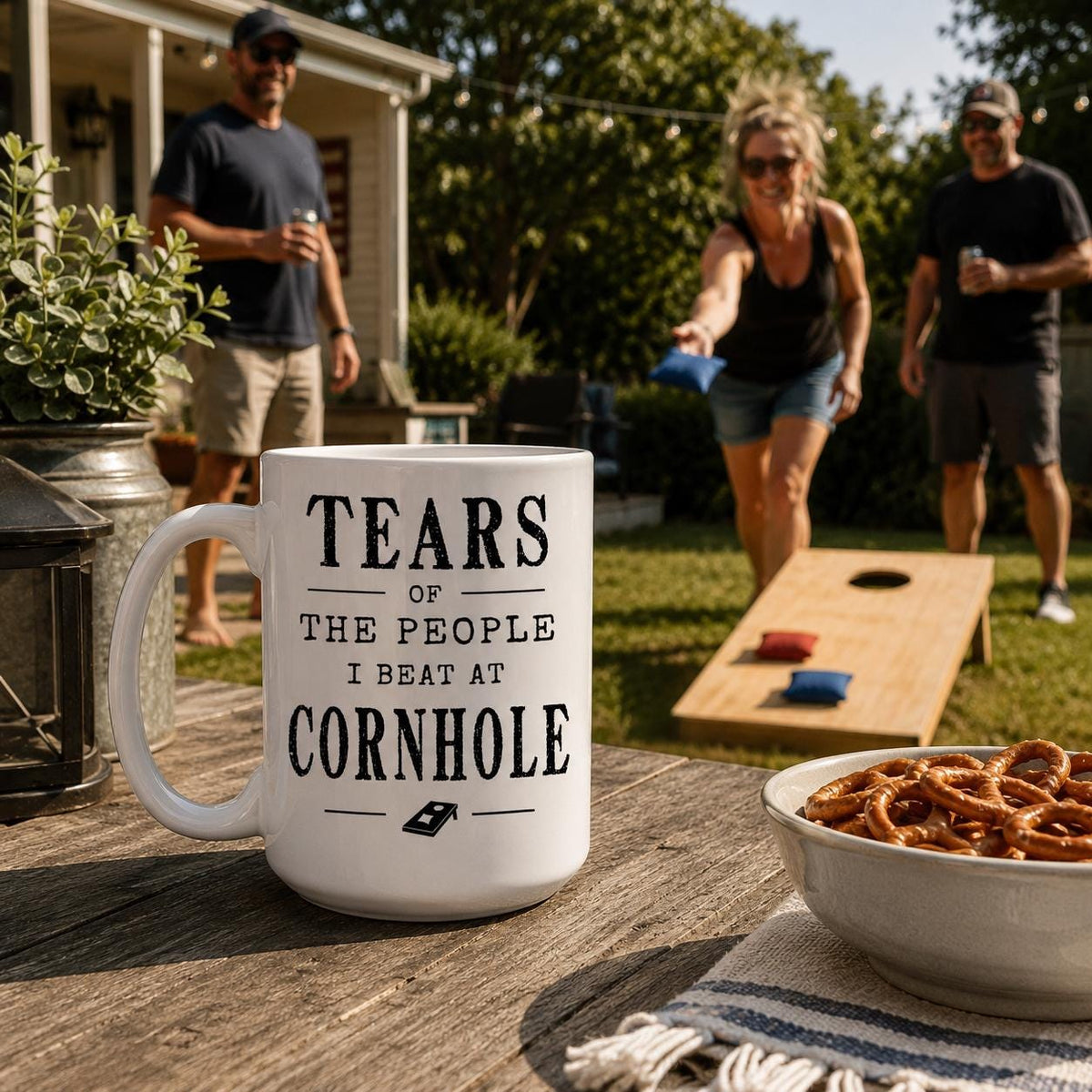 Cornhole mug on a patio table with two people playing cornhole in the background
