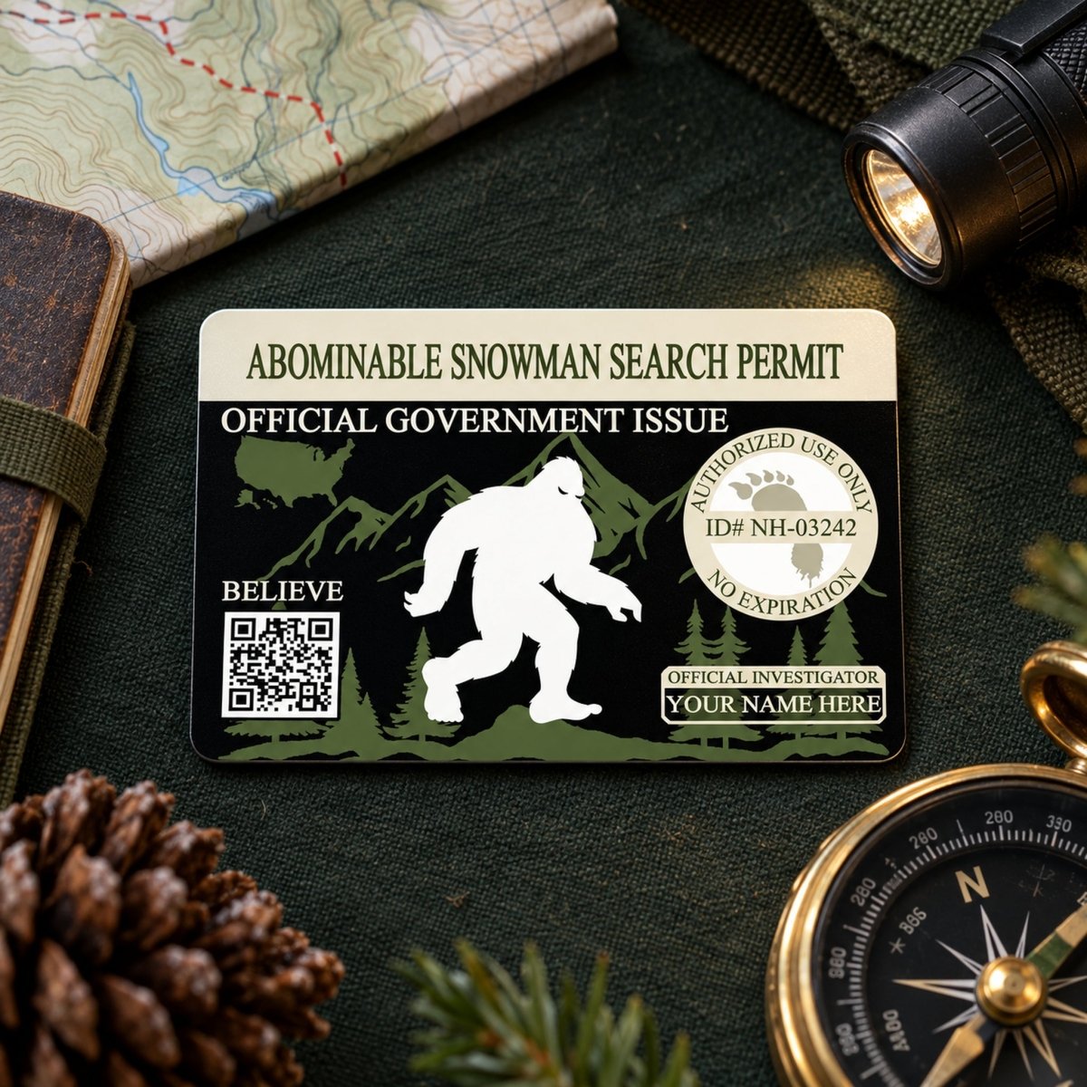 a black and green official government identification card with a white silhouette of a Sasquatch, a mythical creature, printed on it. The card is placed on a table surrounded by various items, including a compass, a magnifying glass, and a pine cone.
