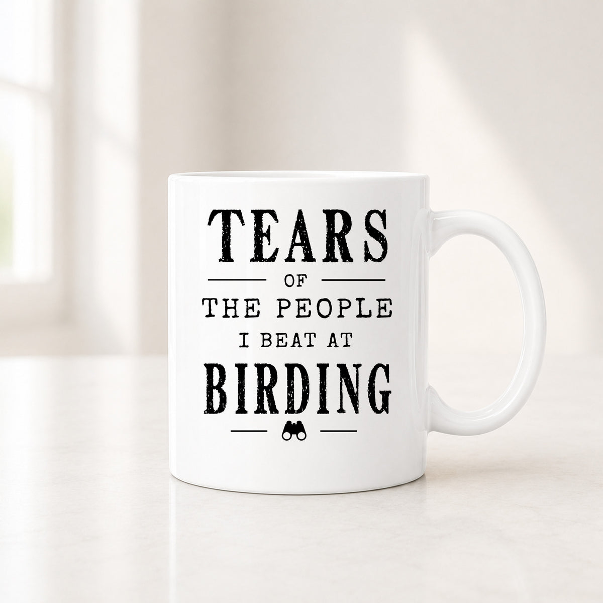 11 oz white birding mug with the black Tears of the People I Beat quote, on a light counter by a window