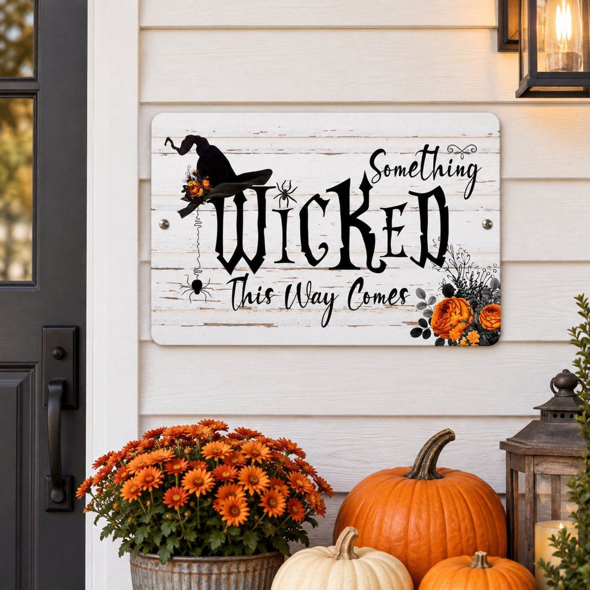 Something Wicked This Way Comes sign on a white wood wall with a witch hat, pumpkins, and flowers