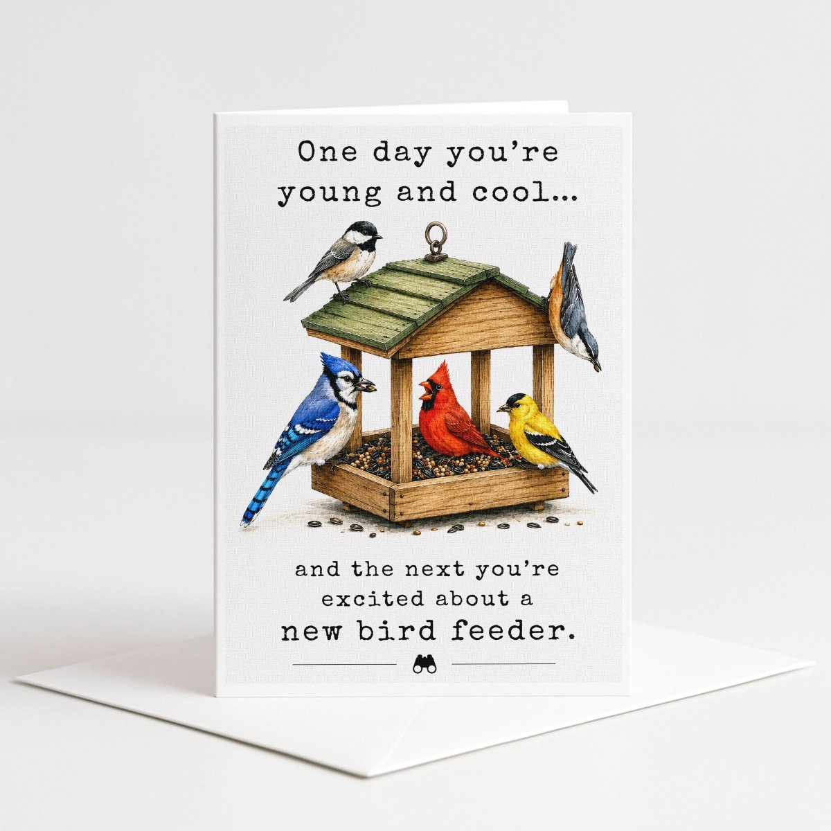A greeting card with a bird feeder illustration and text that reads "One day you're young and cool... and the next you're excited about a new bird feeder."