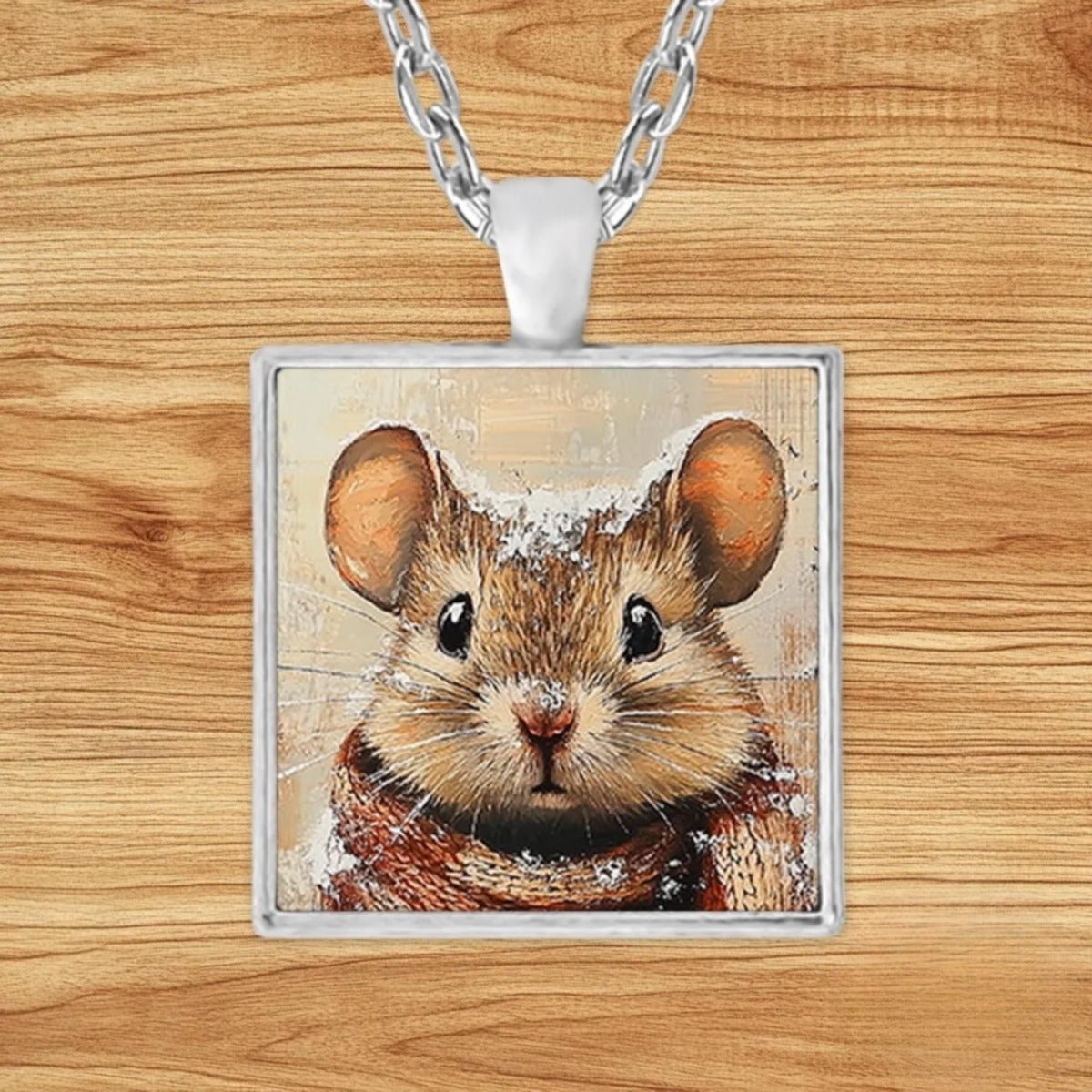 Square silver charm pendant necklace featuring a mouse bundled in a plaid scarf in a snowy forest with a frosted pinecone