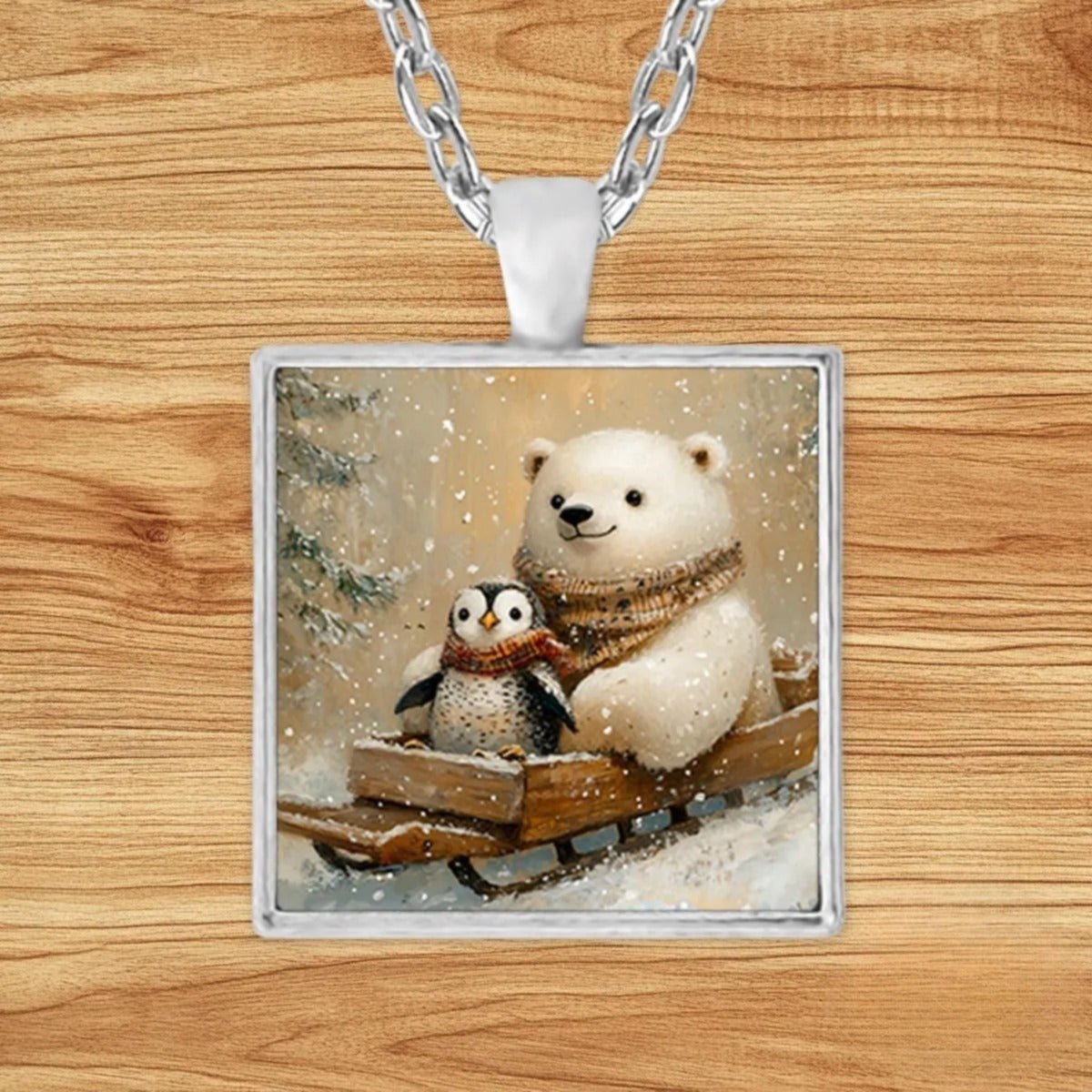 Square silver charm pendant necklace featuring a polar bear and penguin duo riding a wooden sled through a snowy evergreen forest
