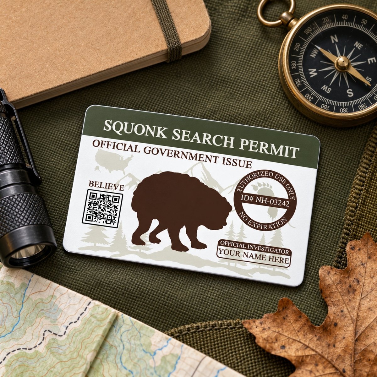 a search permit for a Squonk bear, which is an official government issued permit for bear hunting. The permit is placed on a table surrounded by various items, including a compass, a flashlight, and a leaf.