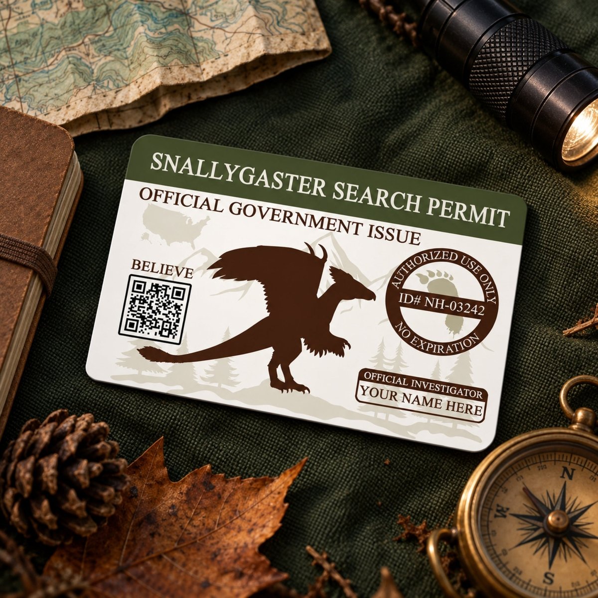 a Snallygaster Search Permit card with a dragon silhouette, placed on a surface with a compass, pine cones, and a map.
