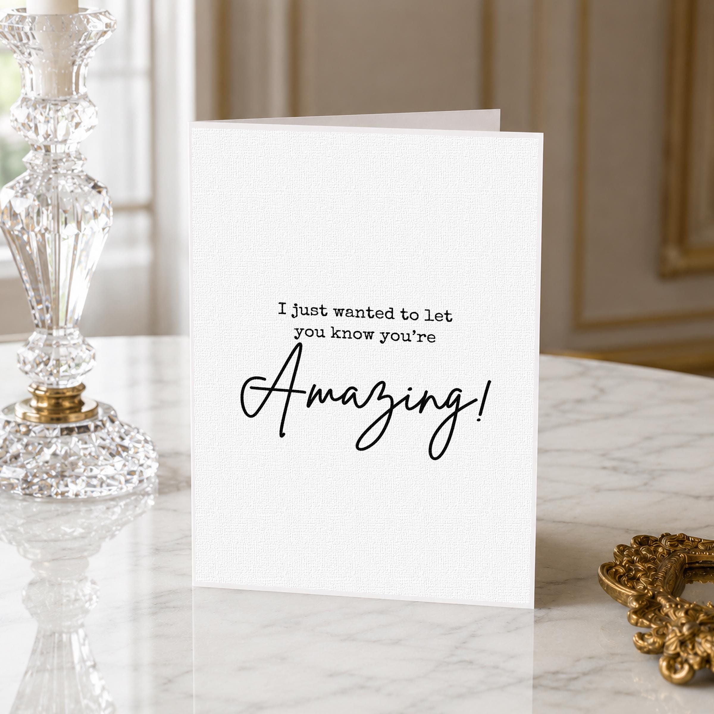 a white card with a message that says "I just wanted to let you know you're Amazing!" placed on a marble surface next to a crystal vase.