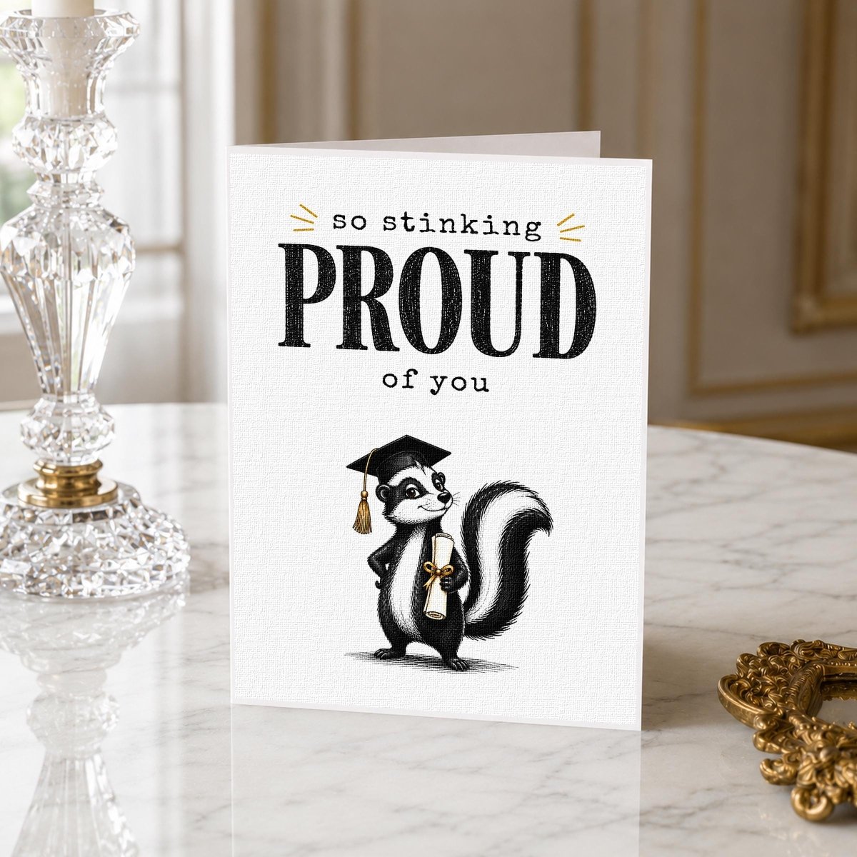 Close-up of the So Stinking Proud Skunk Graduation Card showing the skunk illustration and gold lettering.