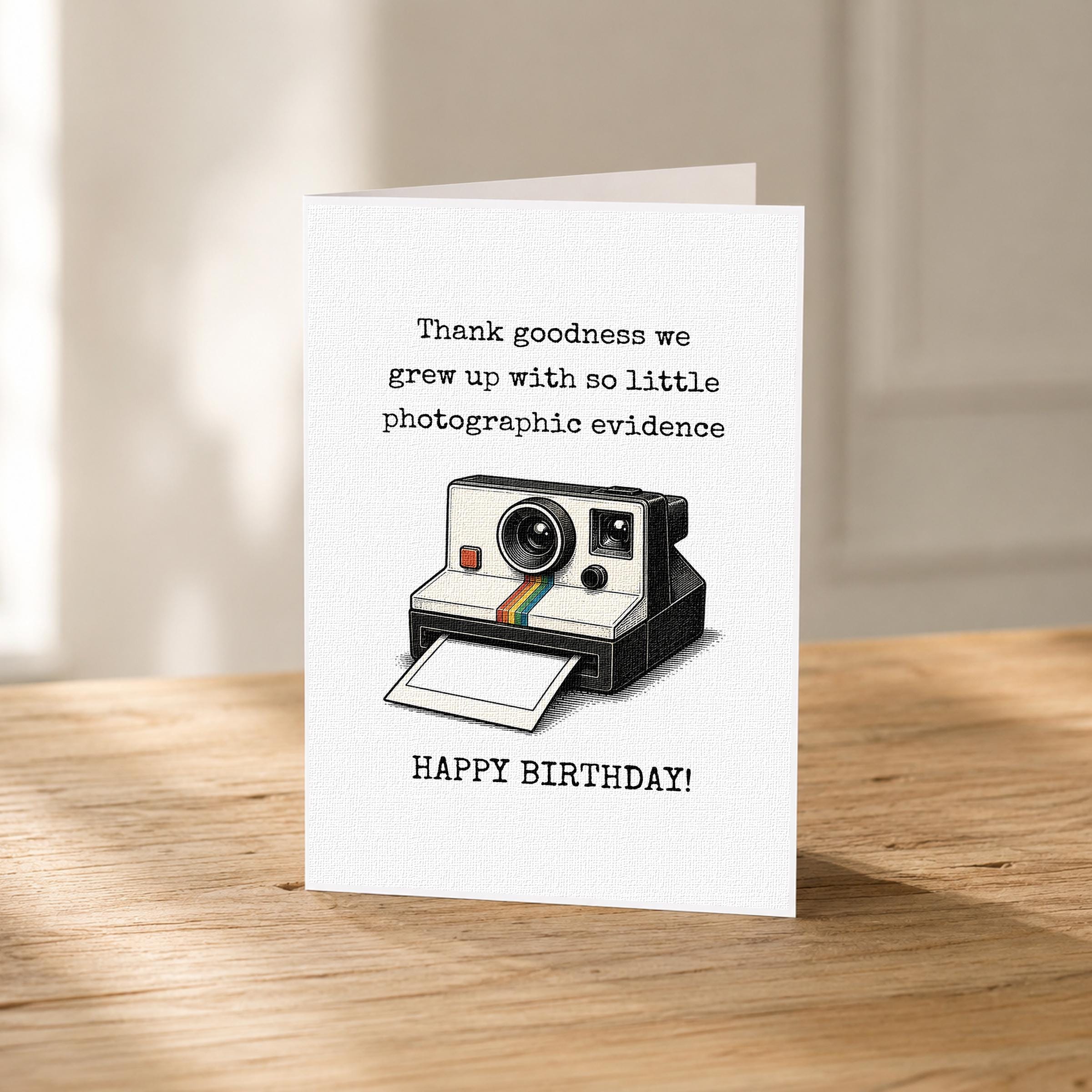 A birthday card with a printed image of a Polaroid camera and text that reads "Thank goodness we grew up with so little photographic evidence" and "Happy Birthday!"