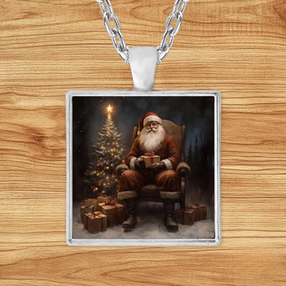 Square silver charm pendant necklace featuring Santa Claus seated in a rocking chair holding a wrapped gift beside a glowing Christmas tree