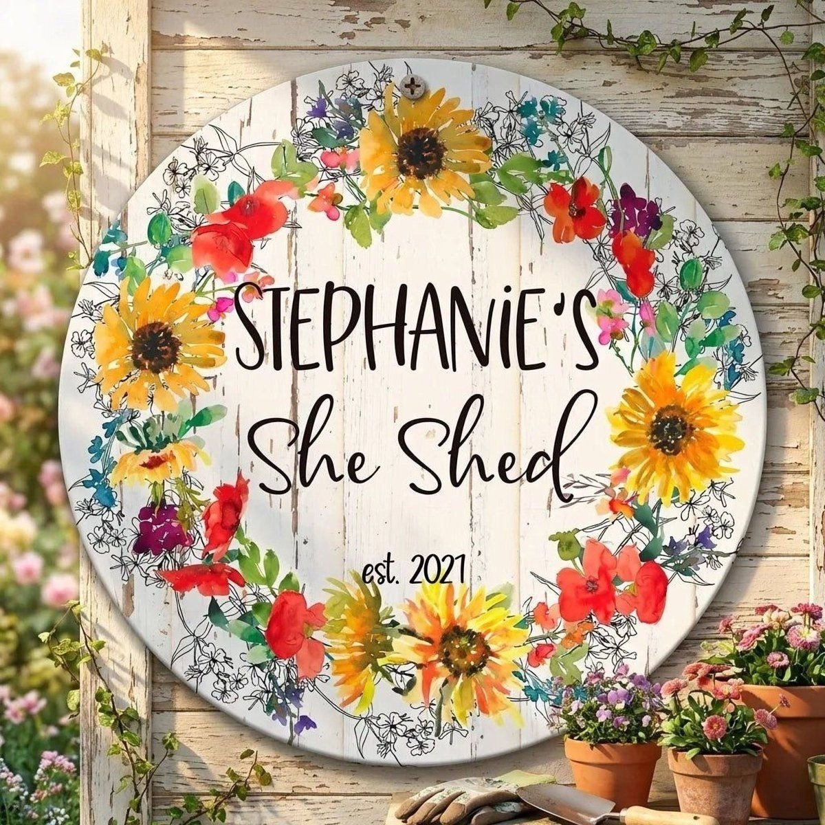 A round sign with a floral wreath design, displaying the name "Stephanie's She Shed" and the year "est. 2021".
