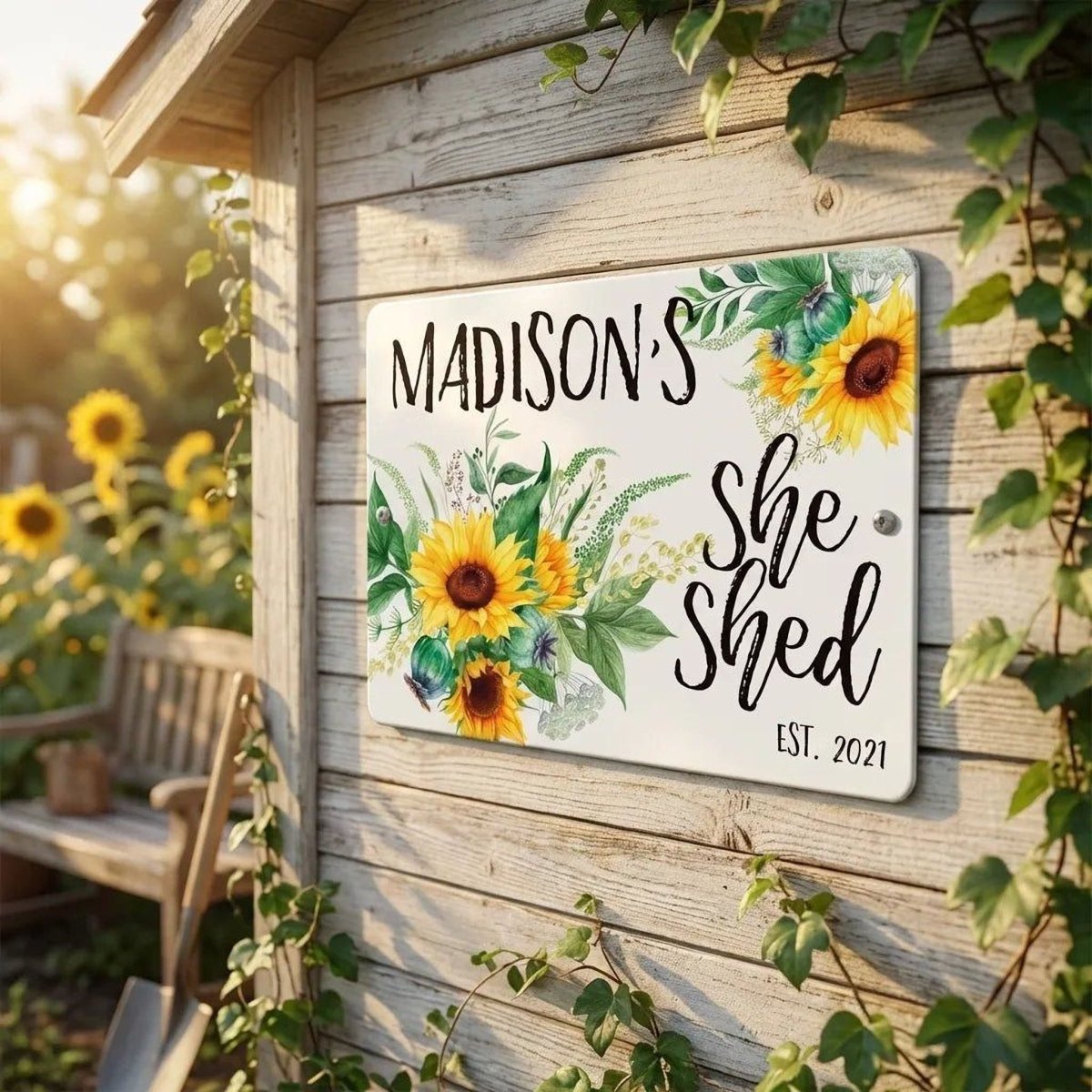A wooden shed with a sign that reads "Madison's She Shed" and "EST. 2021". The sign is decorated with sunflowers and other flowers.