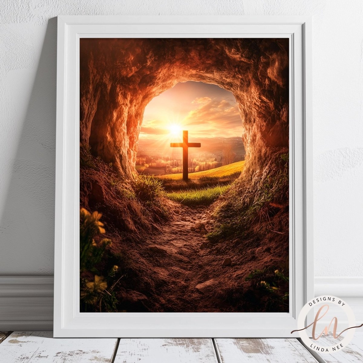 A framed image depicting a cross emerging from a cave, with a sunset sky and landscape in the background.