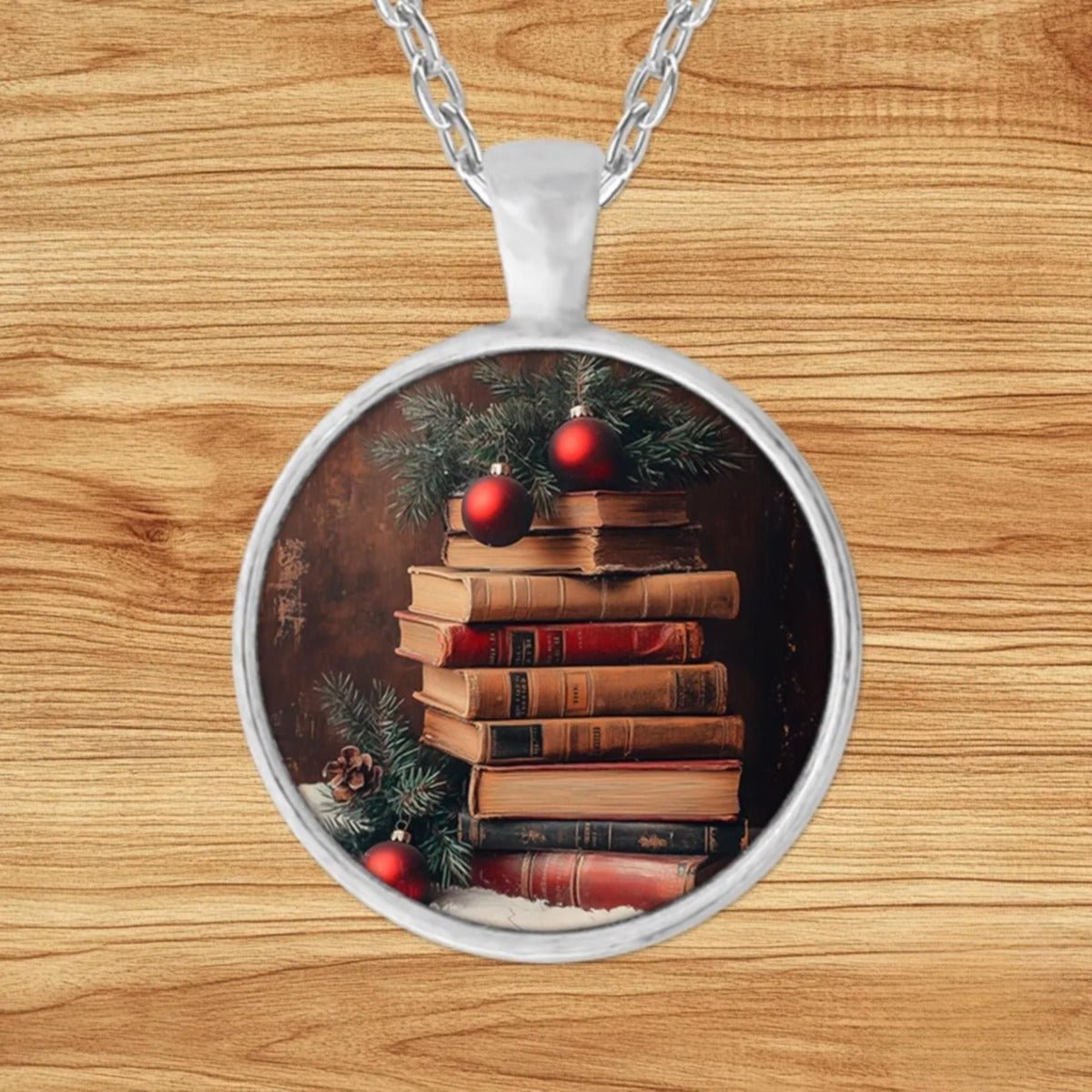 Round silver charm pendant necklace featuring a stack of antique books topped with evergreen sprigs, red ornaments, and snow