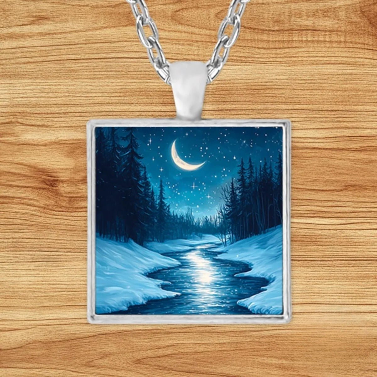 Square silver charm pendant necklace featuring a glowing crescent moon over a snowy pine forest with a frozen, moonlit stream