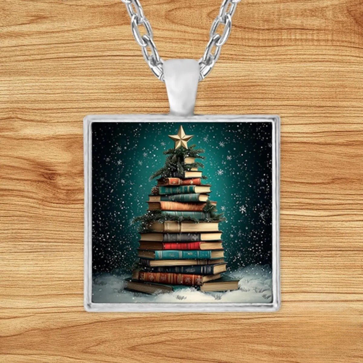 Round silver charm pendant necklace featuring a Christmas tree built from a stack of antique books with evergreen garland and a gold star