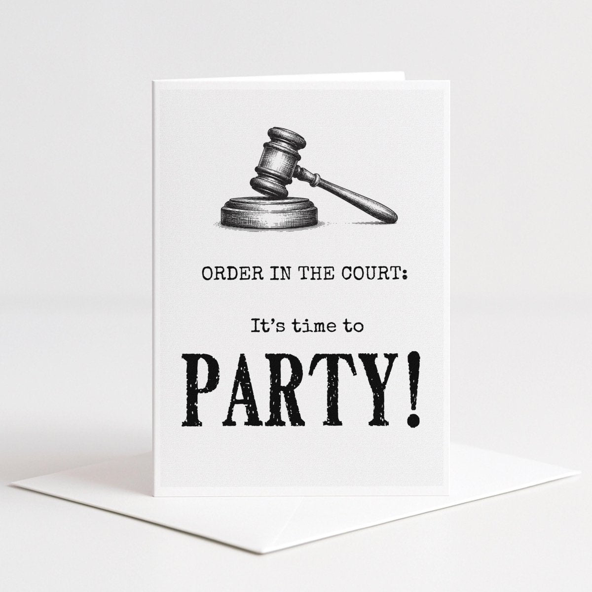 White 5-by-7 greeting card displayed upright on a white envelope with a detailed black gavel illustration and typography reading, “Order in the court: It’s time to party!”