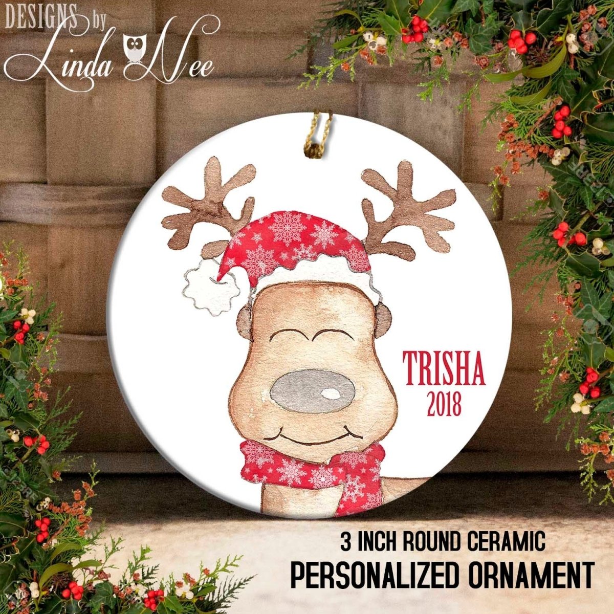 A ceramic ornament featuring a cartoon reindeer wearing a Santa hat and scarf, with the text "TRISHA 2018" and "3 INCH ROUND CERamic PERSONALIZED ORNAMENT" displayed on it.