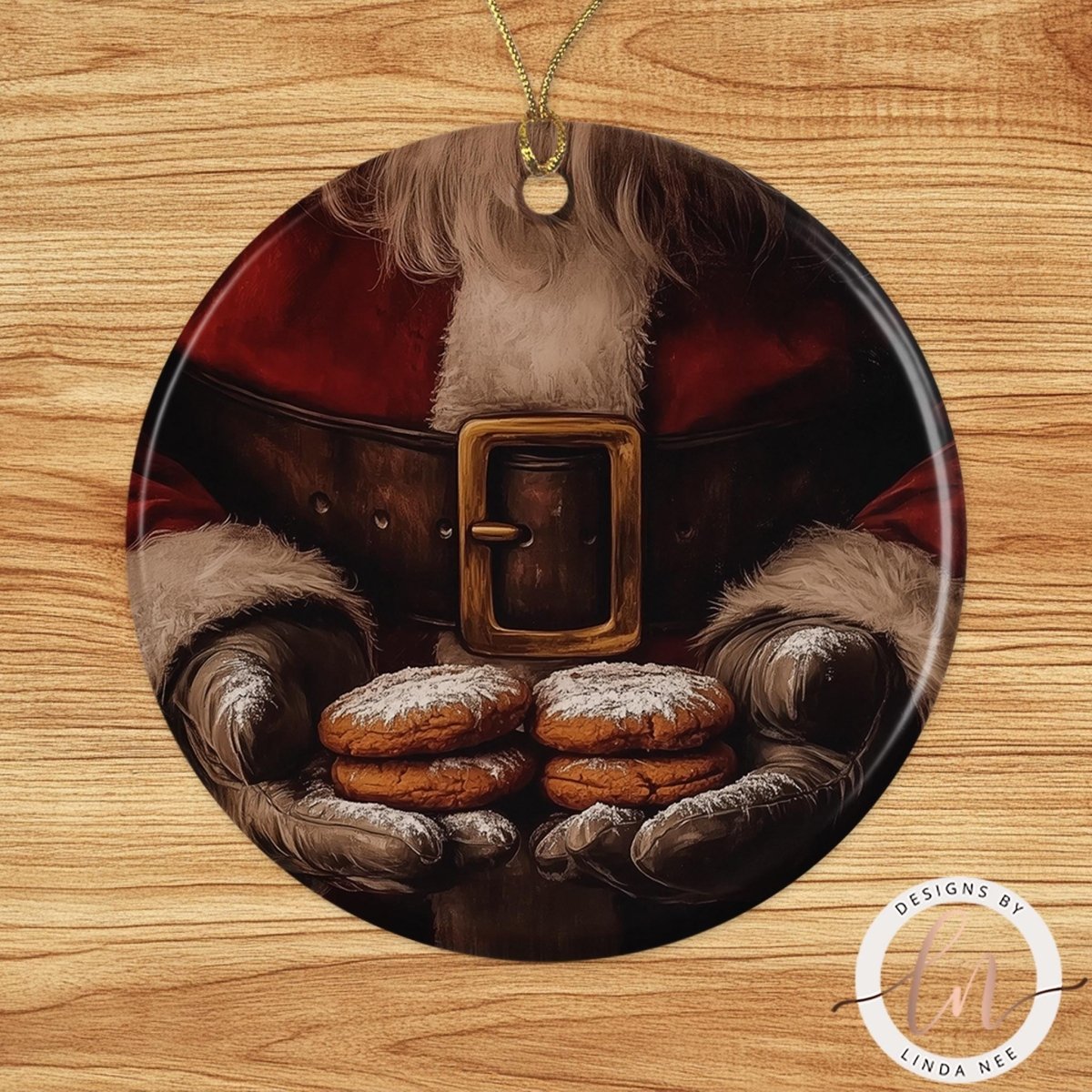 Ceramic ornament showing Santa’s torso in a red suit with black leather gloves holding two powdered cookies, golden belt buckle visible, displayed on wood background. By Designs by Linda Nee.