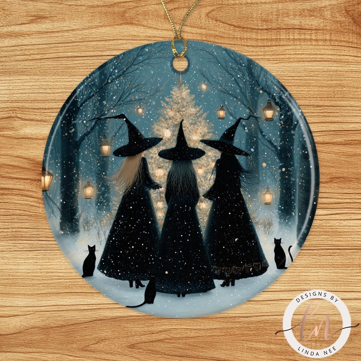 A round ornament featuring three black-haired women wearing black dresses and black hats, standing in a snowy forest with a Christmas tree in the background.