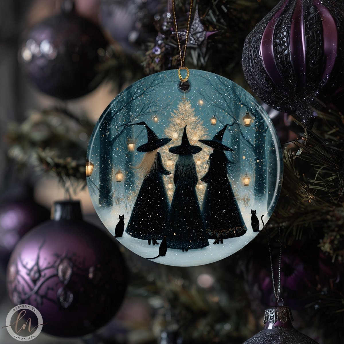a round ornament hanging on a Christmas tree, depicting three black-haired women wearing black dresses and witch hats, with a snowy forest scene in the background.
