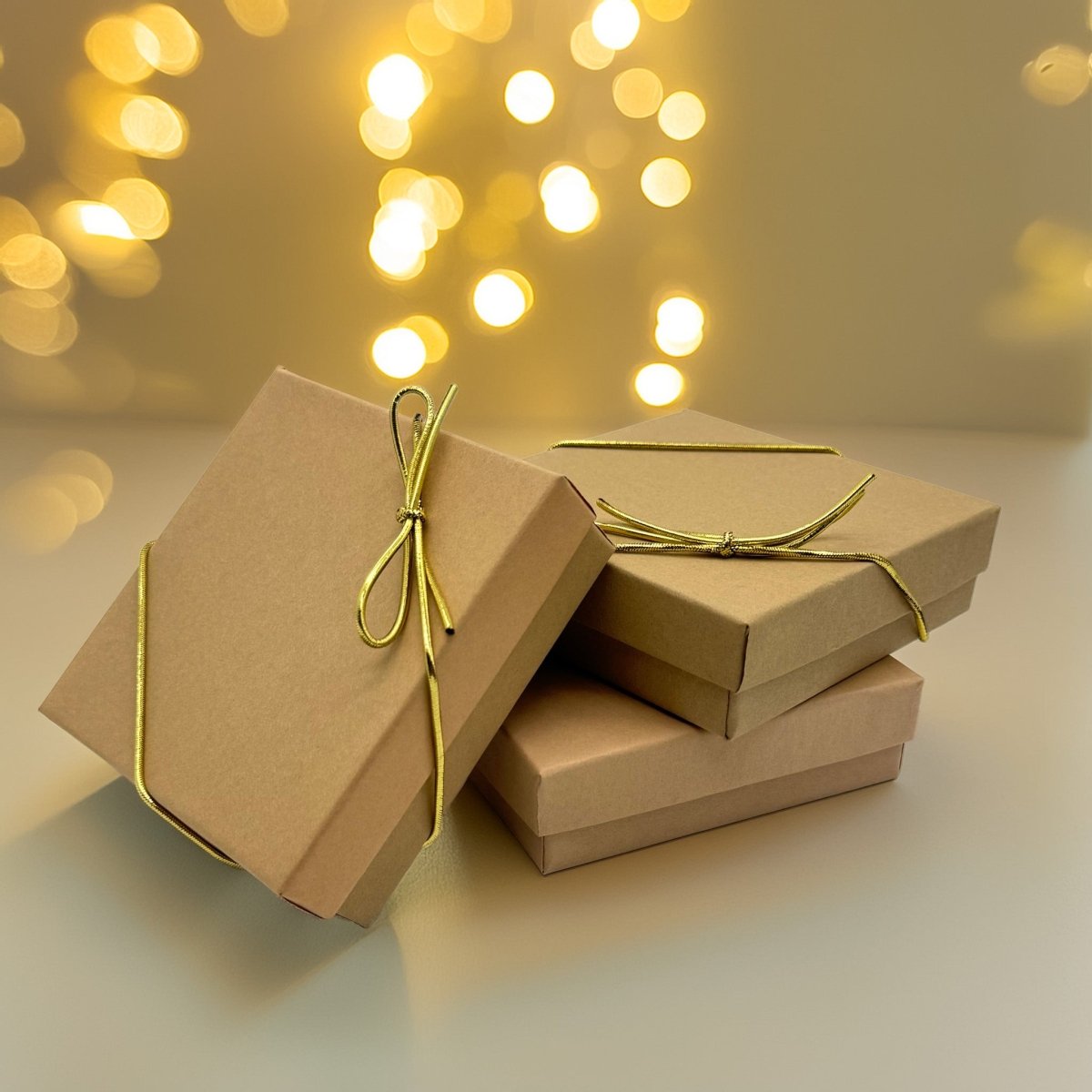 A stack of brown gift boxes with gold ribbons tied around them, set against a background of blurred, warm-toned lights.
