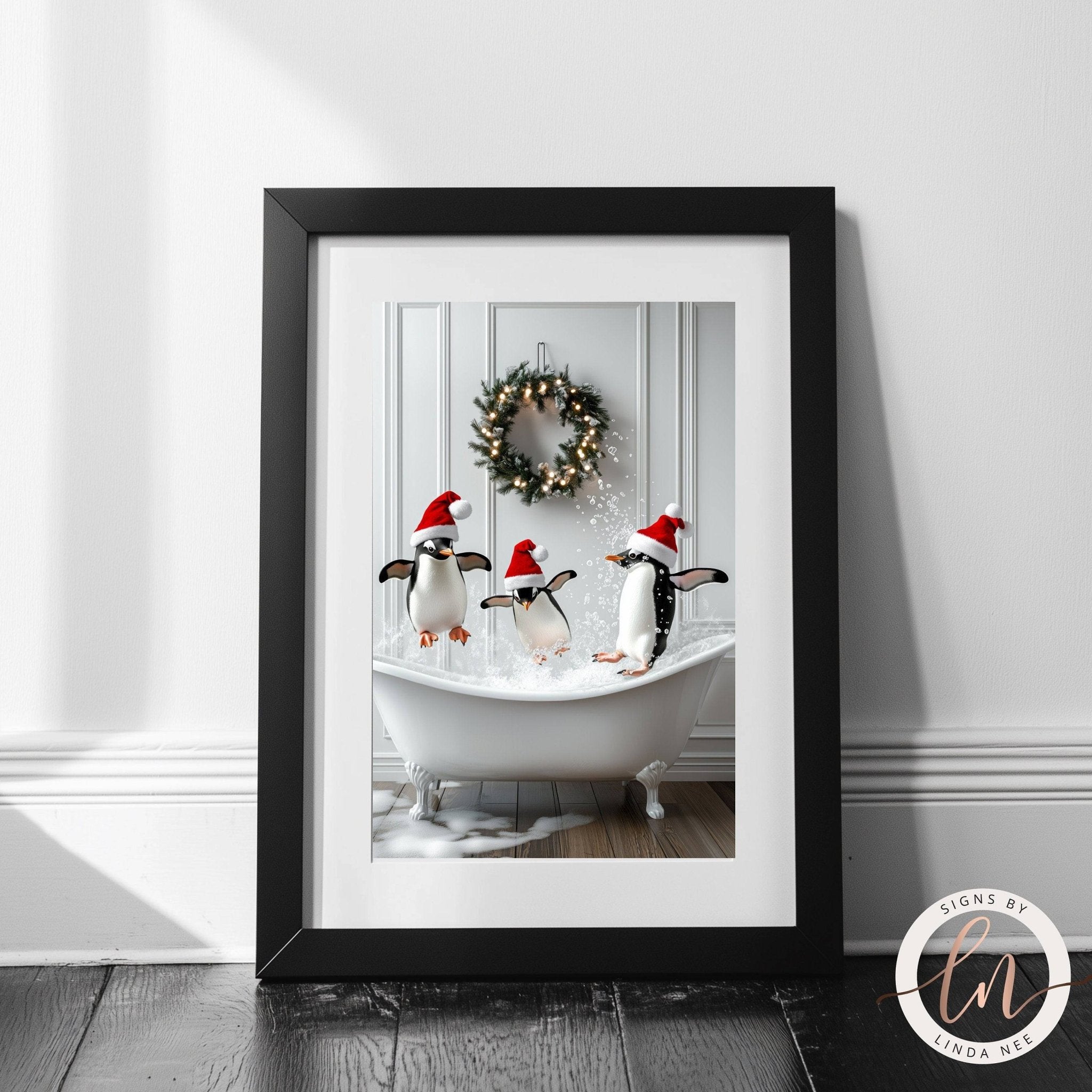 A framed image of three penguins wearing Santa hats, standing in a bathtub filled with water, with a wreath hanging on the wall behind them.