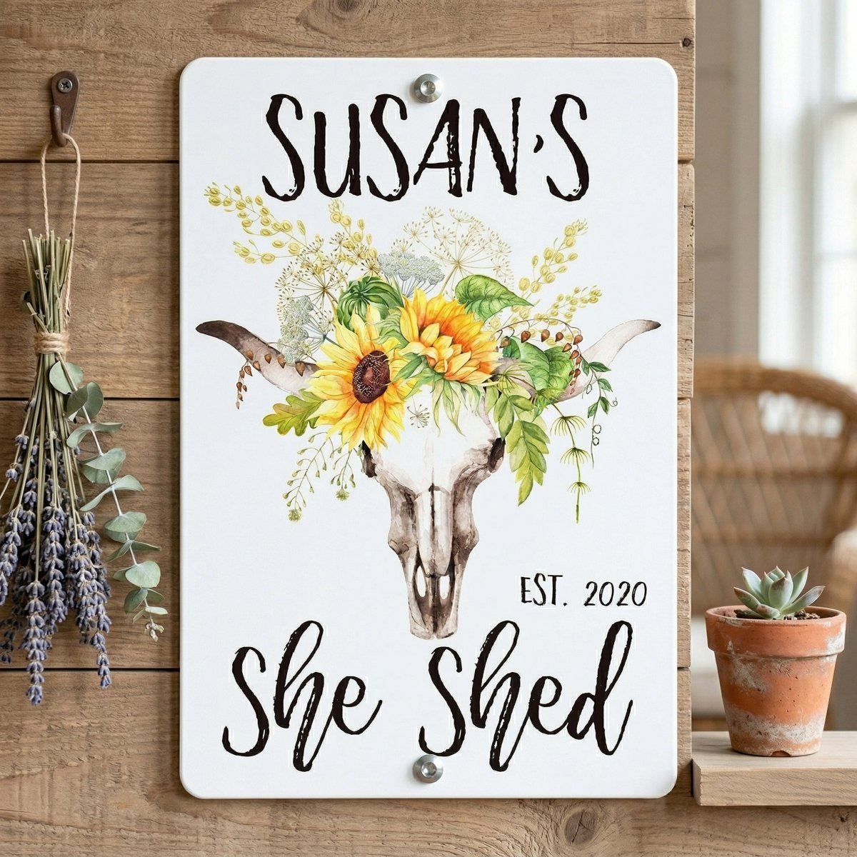 A white sign with a painted skull and floral arrangement, hanging on a wooden wall.