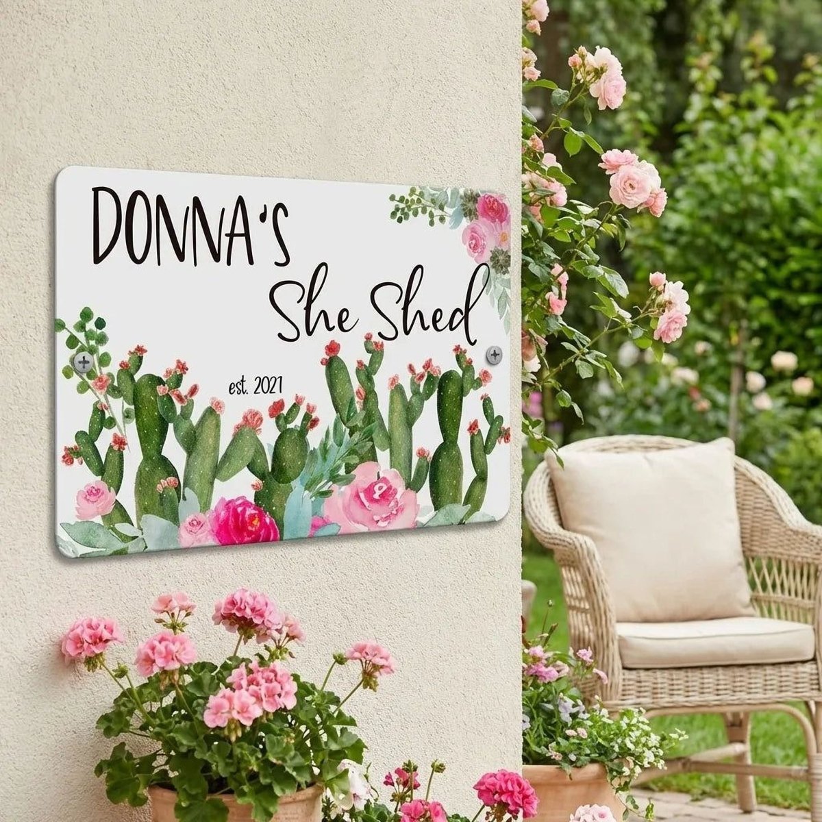 a sign that reads "DONNA'S She Shed" with a floral design, hanging on a wall next to a wicker chair and a potted plant.