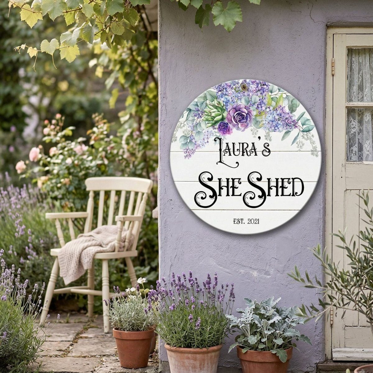 A round sign on a wall that says "LURA'S SHED" with a floral design, surrounded by potted plants and a wooden chair in a garden setting.