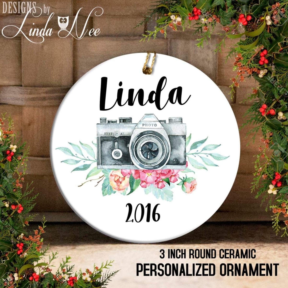 Round ceramic personalized ornament with camera design and floral elements, featuring the name 'Linda' and the year '2016'.