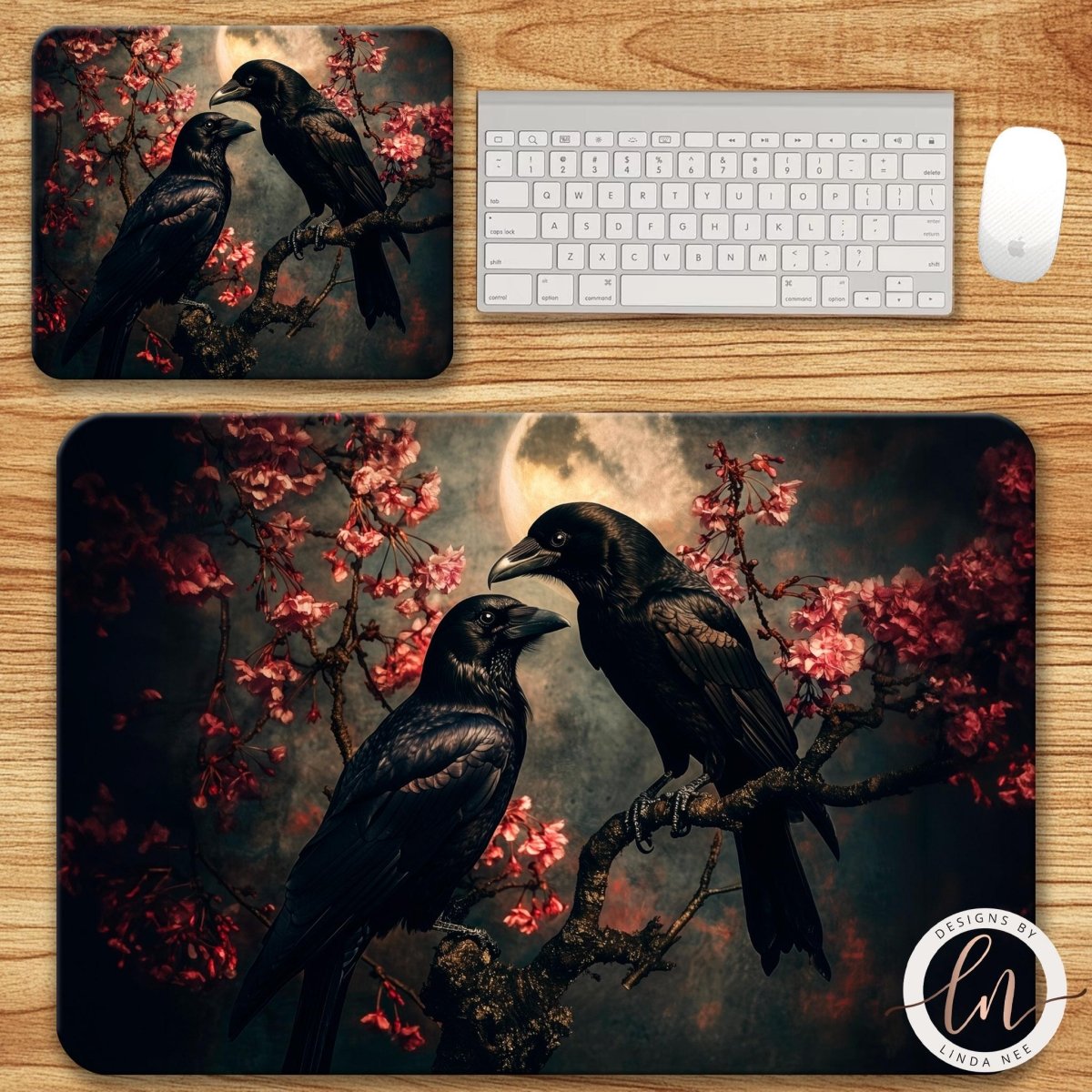 Two mouse pads with crows and cherry blossoms on a wooden desk with a keyboard and mouse.