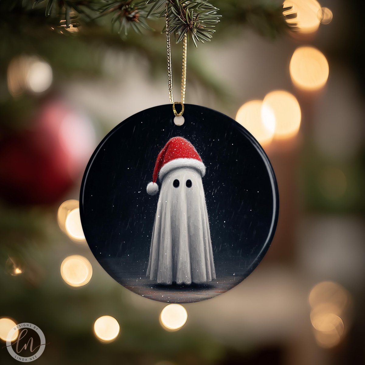 A round ornament featuring a ghost wearing a Santa hat, hanging from a tree branch with a blurred background of lights.