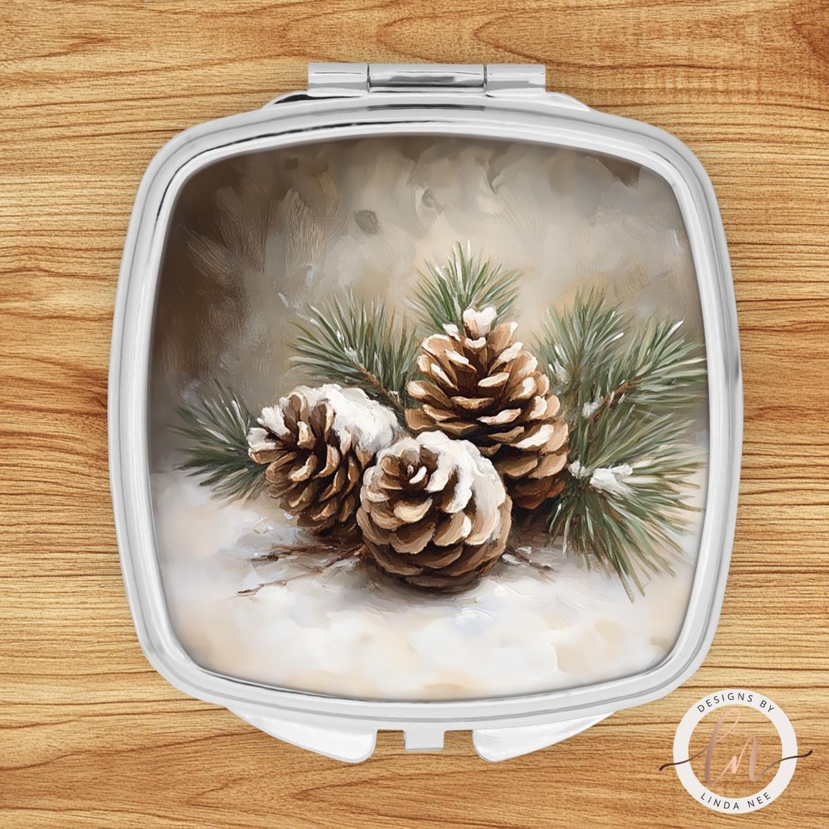 A square mirror with a painting of pine cones and pine needles on its surface, set against a snowy background.