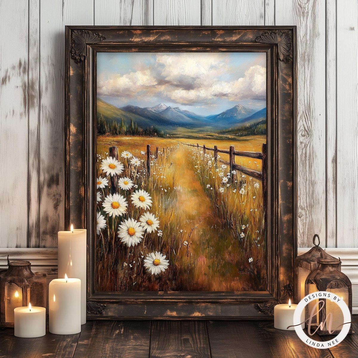 a framed painting of a field with white daisies, a wooden fence, and mountains in the background. The painting is displayed on a wooden surface, with three lit candles and lanterns in the foreground.