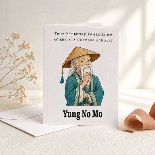 Funny birthday greeting card featuring a wise Chinese scholar, styled with an envelope, dried flowers, and warm neutral decor.