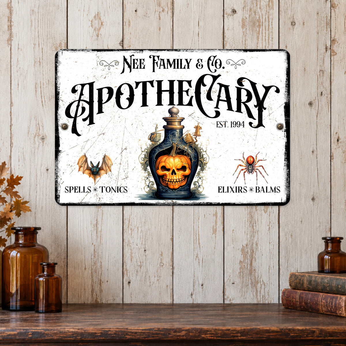 A rectangular vintage-style metal wall sign with a distressed white background and gothic text reading 'Nee Family & Co. Apothecary' above an illustrated skull in a glass bottle, displayed against a rustic wood plank wall above a wooden shelf with amber bottles and books.