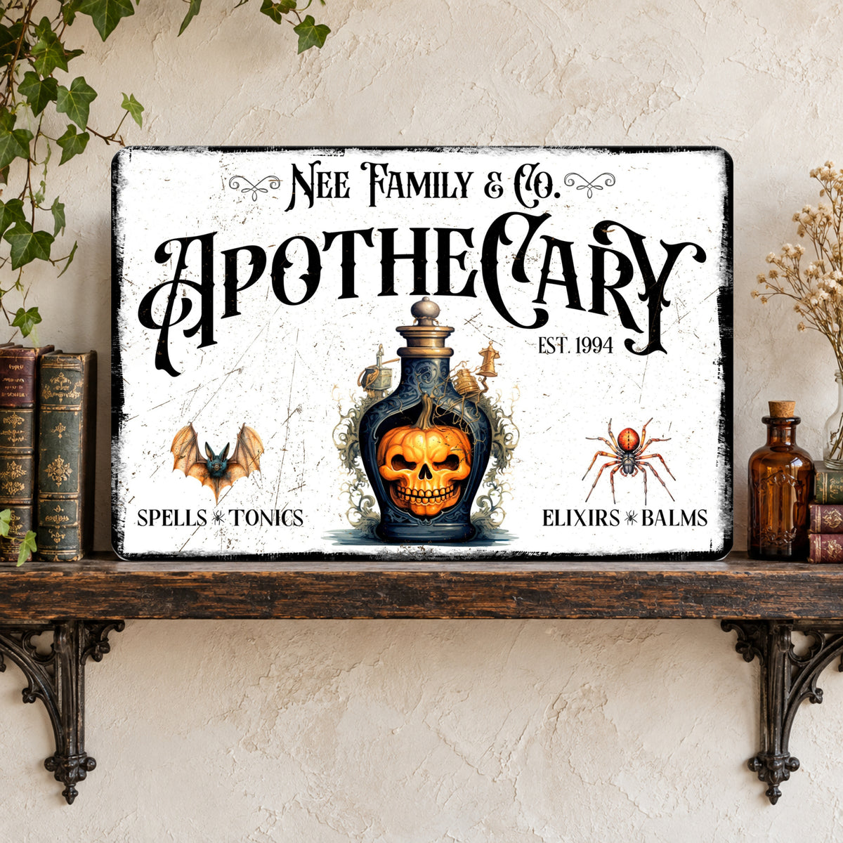 A rectangular vintage-style Apothecary sign with a distressed white background, black gothic lettering, and Halloween-themed illustrations including a skull in a potion bottle, bat, spider, and potion pot. The sign is displayed on a dark wooden shelf against a textured beige wall with decorative books and dried flowers.