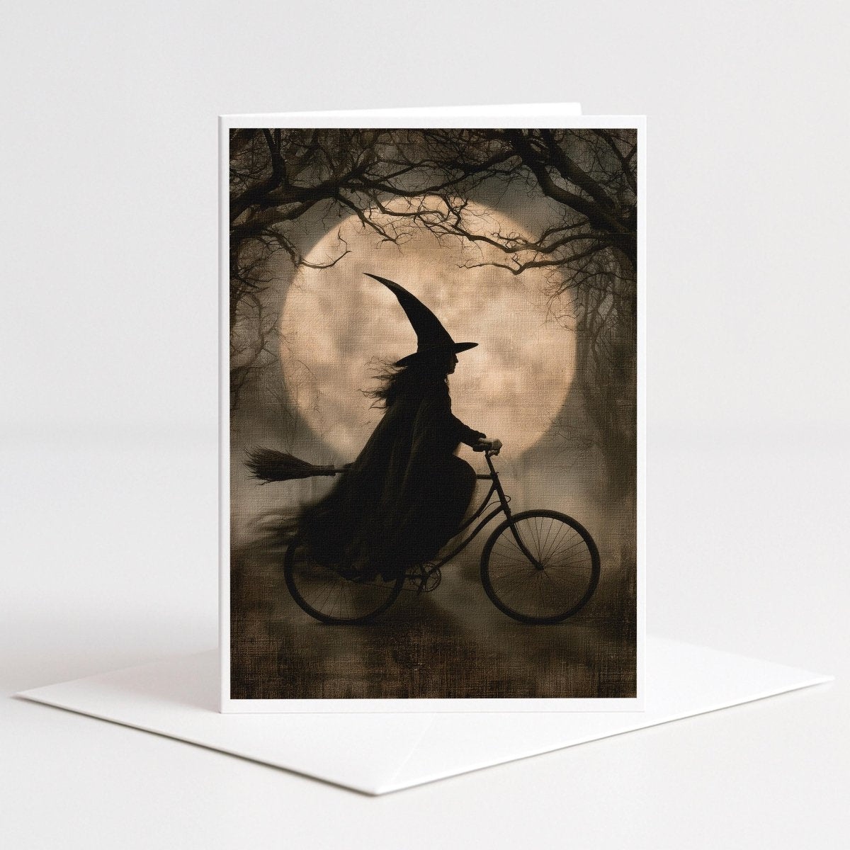 Vintage sepia note card art of a witch with flowing hair riding a bicycle past a pale full moon