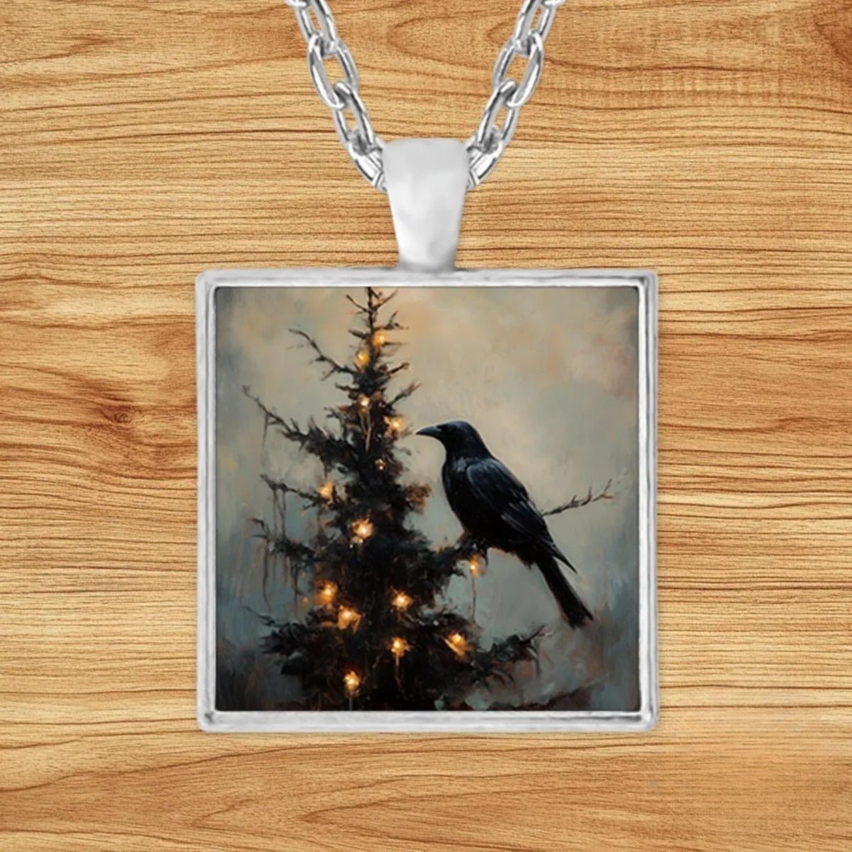 Square silver charm pendant necklace featuring a black raven perched on an evergreen tree dripping with golden candle-like lights