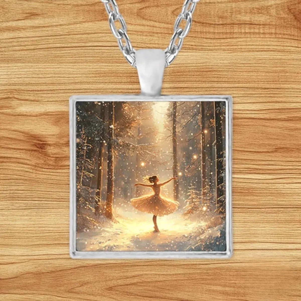 Square silver charm pendant necklace featuring a ballerina mid-pose in a snow-covered forest with golden light and falling snowflakes