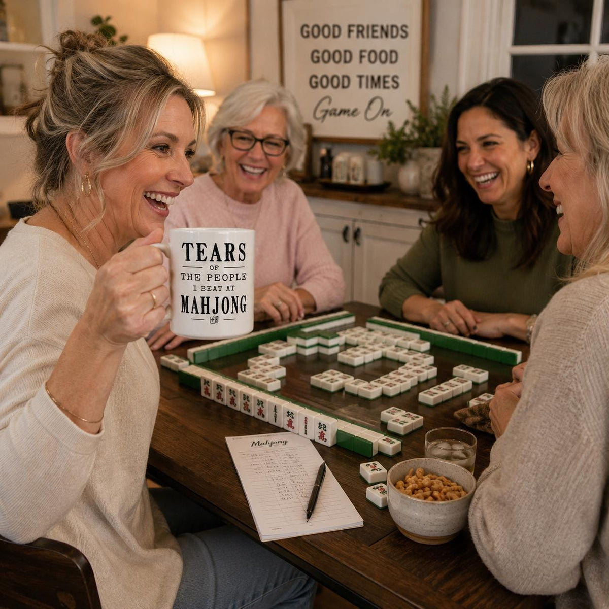 Four women laughing around a mahjong table while one holds the Tears of the People I Beat at Mahjong mug